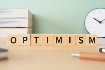 楽観主義のイメージ｜「OPTIMISM」と書かれたブロックが置かれたデスク
