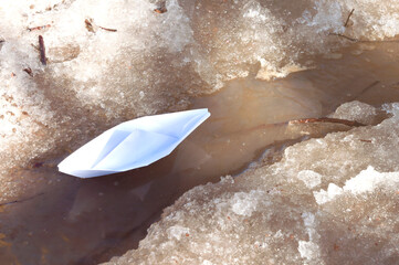 A white paper boat sails along a spring stream among the snowy shores
