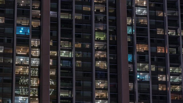 Big glowing windows in modern office and residential buildings timelapse at night, in rows of windows light shines. Many blocks of apartments