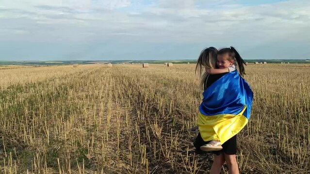 Woman and child with Ukrainian flag. War in Ukraine. Russian aggression in Ukraine. Stop war. Children against war. Ukrainian children. Mother and daughter are walking across the field. 