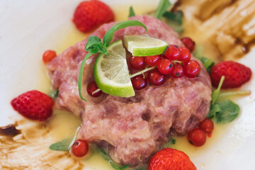Delicious meat lovers' dish - dry aged beef tartare with anchovy, capers, lime, soy sauce, red currant and fresh strawberry