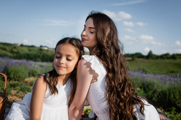 woman and child with long hair and closed eyes sitting in blurred meadow.