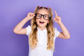 Photo portrait of adorable excited small girl tails eureka finger point up wear stylish white uniform isolated on violet color background - obrazy, fototapety, plakaty