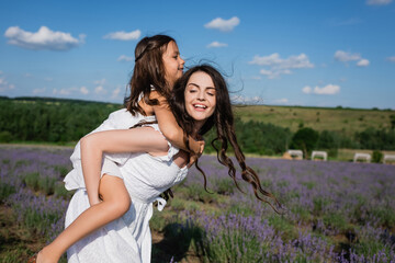cheerful brunette woman piggybacking daughter in flowering field.