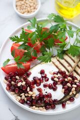 Grilled slices of aubergine served with pomegranate seeds, pine nuts, yogurt, red tomatoes and parsley, closeup, vertical shot