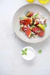 Plate with grilled watermelon batons, grated cheese and yogurt, above view on a light-beige marble background, vertical shot with space