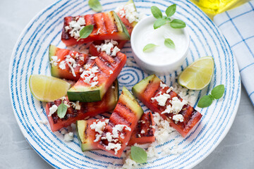 Grilled watermelon with grated cheese, white yogurt and lime served on a blue and white plate, middle closeup, selective focus