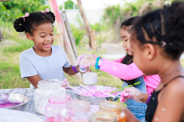 Lovely Asian and African girls making and play colorful dough together at playground, summer camp...