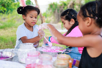 Lovely Asian and African girls making and play colorful dough together at playground, summer camp learning