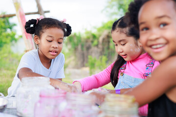 Lovely Asian and African girls making and play colorful dough together at playground, summer camp...