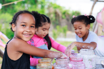 Lovely Asian and smiling African girls making and play colorful dough together at playground,...