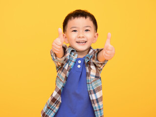 happy little boy in front of yellow background and showing thumbs up