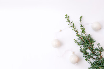 Fototapeta na wymiar White garland. New Year's decoration and a branch of a Christmas tree or juniper on a white background in one corner of the photo. Round balls with ribbon. Flat Lay. Copy space. Soft selective focus.