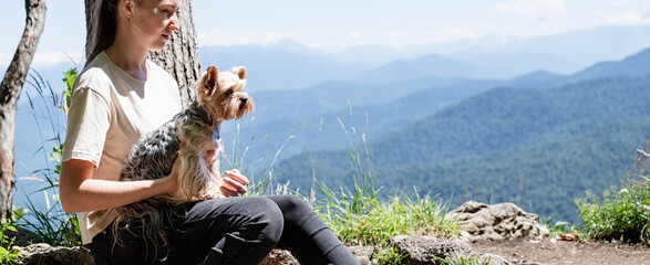 young woman holding small dog puppy yorkshire terrier hiking at the mountains