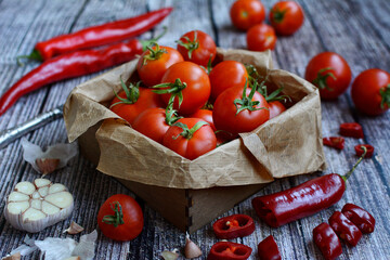Closeup of a wooden box with ripe tomatoes, hot chili peppers, garlic on a wooden background. Season, harvest. Healthy food preparation