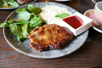 pork steak with sauce and herbs on a plate on a wooden table
