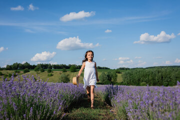 full length of smiling girl in white summer dress walking in meadow of blooming lavender.