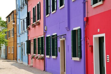 Fototapeta na wymiar colourful houses in Burano, houses painted in strong colours, small colourful houses, flowers in windows, fabric curtain on front door, blue, violet and pink house, typical architecture, Italy, Veneto