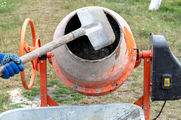 A worker shovels sand into a concrete mixer, preparing cement mortar