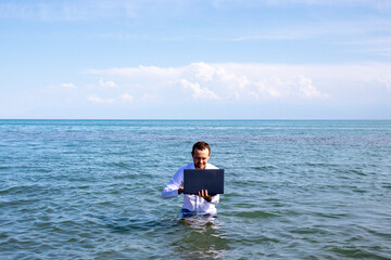 a guy with a laptop in the sea in a white office shirt. work on vacation.