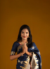 Portrait of a beautiful Indian girl in a greeting pose to Namaste hands. India woman in traditional saree.