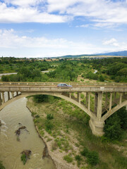 Fototapeta na wymiar Car rides on an old arch bridge over a mountain river on a summer day, a side view from a drone