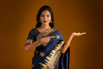 Portrait of Indian traditional young woman or girl presenting something, showing copy space on her palm on a brown background