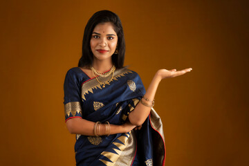 Portrait of Indian traditional young woman or girl presenting something, showing copy space on her palm on a brown background