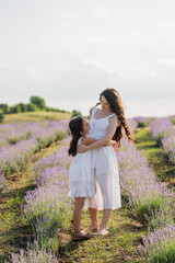 full length of brunette mom and daughter in white dresses embracing in meadow.