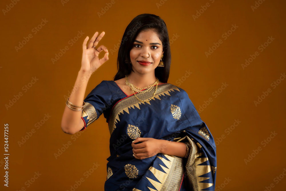 Wall mural young smiling girl showing ok sign on a brown background