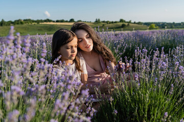 brunette woman and girl sitting in lavender field on summer day.
