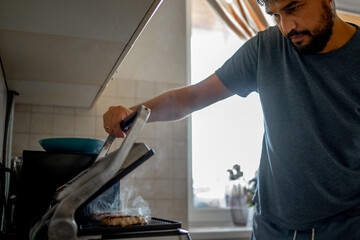 Fototapeta na wymiar a man at home in the kitchen cooks cutlets on the grill
