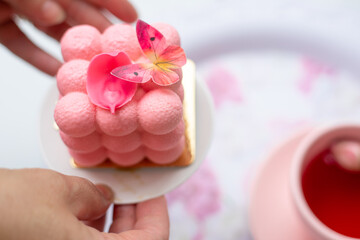 Close up pink neo cube ball velours mousse cake dessert with petals and butterfly on plate in hands...