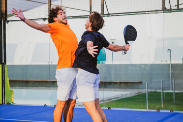 Portrait of two smiling sportsman's posing on padel court outdoor with rackets - Padel players  embracing after win a padel match