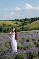Fototapeta na wymiar pretty woman in white dress looking away in field with blossoming lavender.