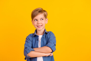 Photo of smart creative minded boy folded arms toothy smile look empty space isolated on yellow color background