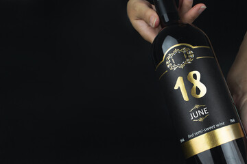 June 18th. Day 18 of month, Calendar date. Hands hold bottle of red wine with a calendar date on label.  Summer month, day of the year concept.