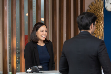 beautiful young asian woman receptionists working at a reception desk and holding credit card for customer paying.