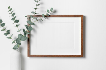 Blank landscape frame mockup for artwork or print on white wall with eucalyptus plant in vase