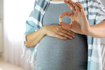 Pregnant woman at home hold pill in hand. Baby expectation, health care and prenatal vitamins on...