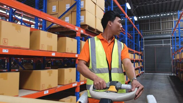 Asian male warehouse worker driving hand pallet truck in warehouse