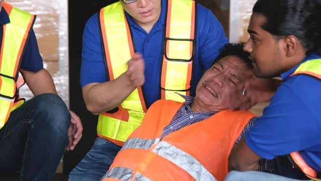 Colleagues provide first aid to a porter of an elderly Asian man who has fainted or a heart attack while working in a warehouse.