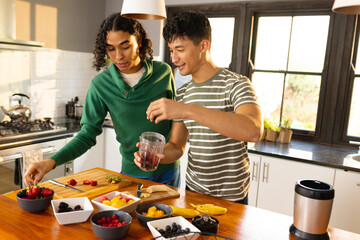 Happy biracial lgbt male couple preparing healthy drink together in kitchen