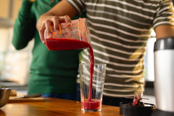 Happy biracial lgbt male couple preparing healthy drink together in kitchen