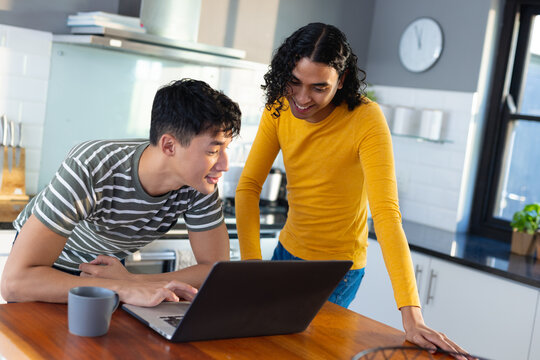 Happy biracial lgbt male couple using laptop in kitchen together - Powered by Adobe