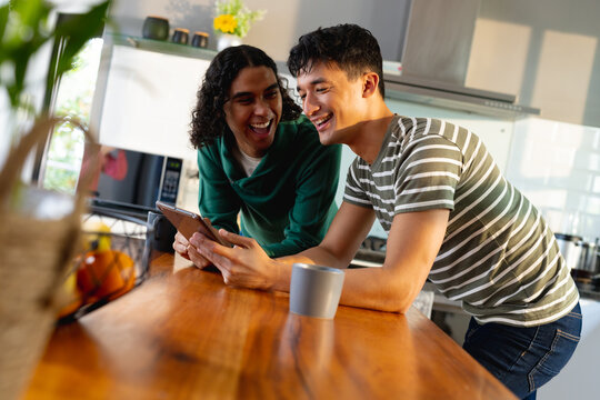 Happy biracial lgbt male couple using tablet in kitchen together