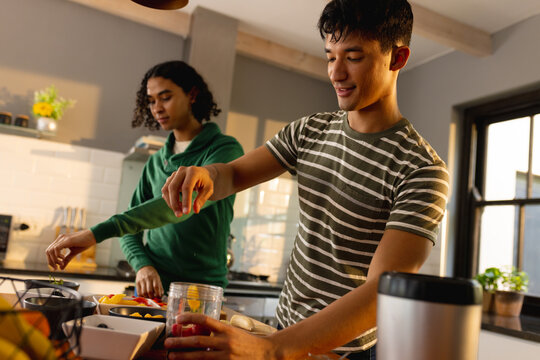 Happy biracial lgbt male couple preparing healthy drink together in kitchen