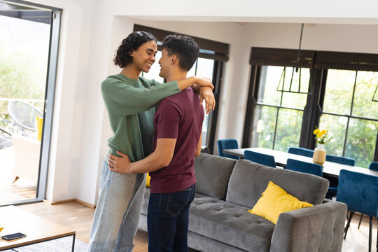 Happy biracial lgbt male couple embracing and smiling in living room