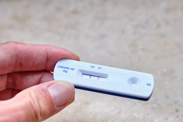 Male hand holding a positive COVID-19 rapid antigen test between the fingers. Seen in Germany in...