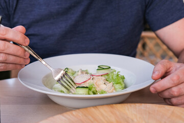 A man eats a salad with squid, cucumbers and greens with oyster sauce in a cafe